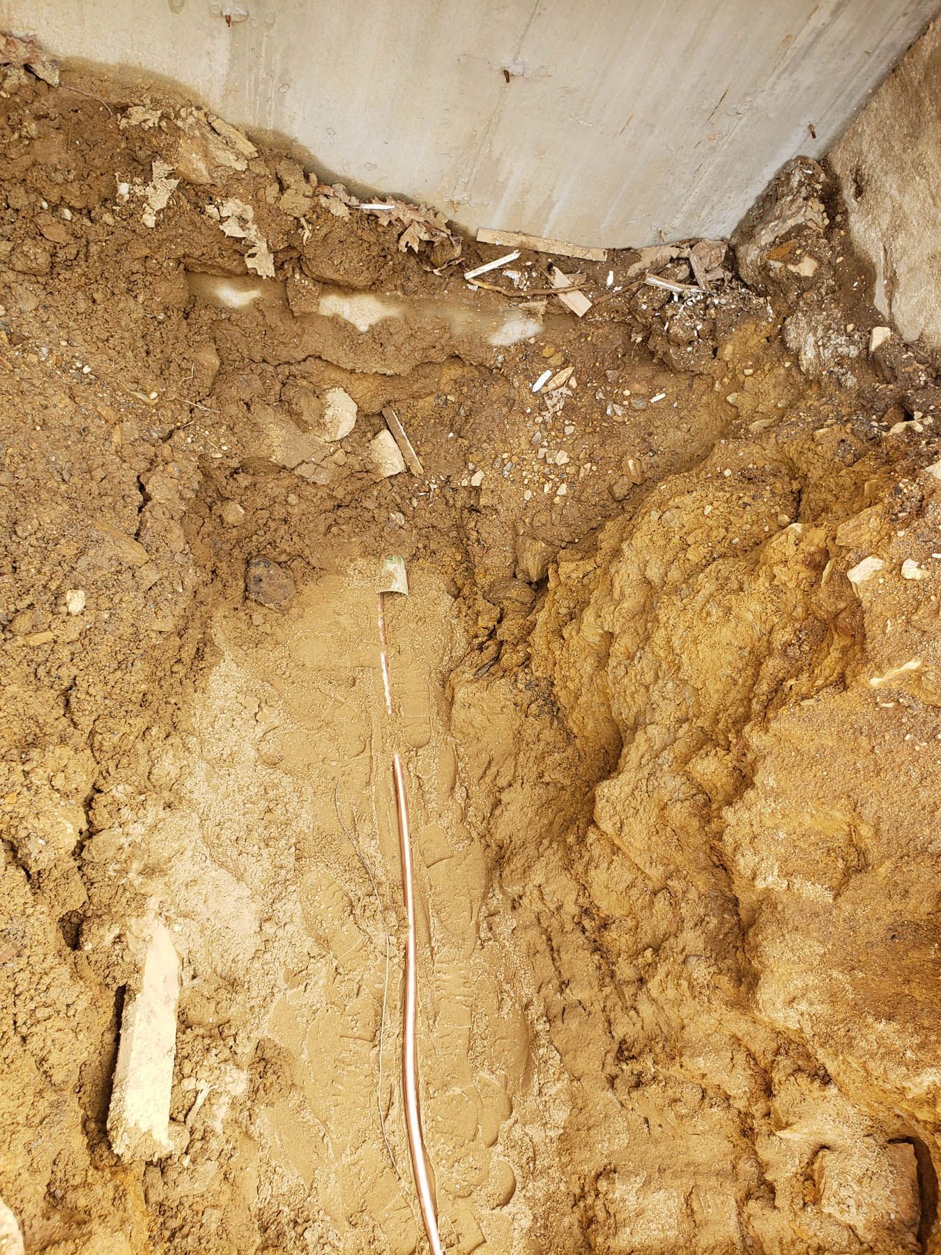 Soil excavated next to a concrete wall; dark brown and tan earth layers.