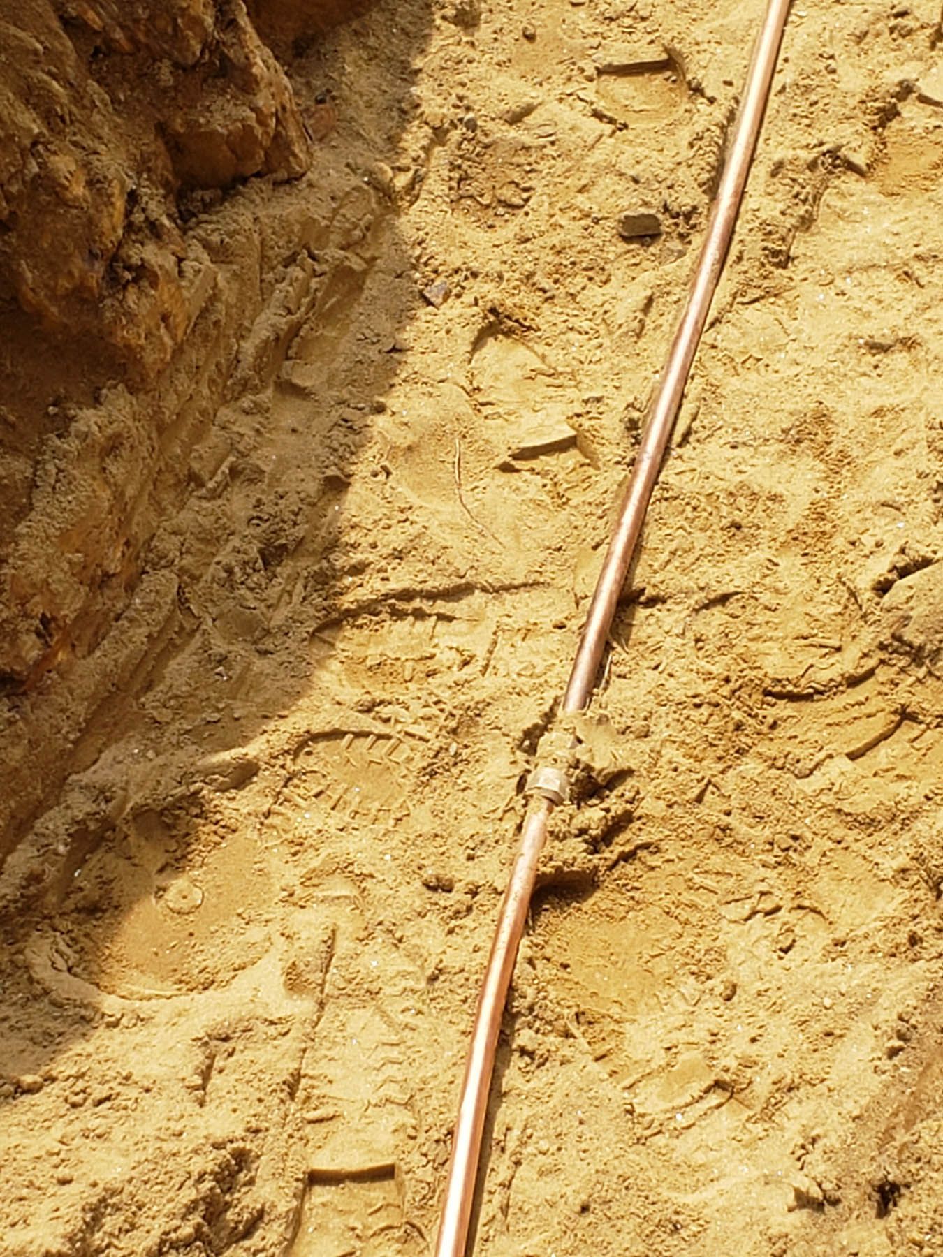 Copper pipe in a sandy trench, possibly for electrical grounding.