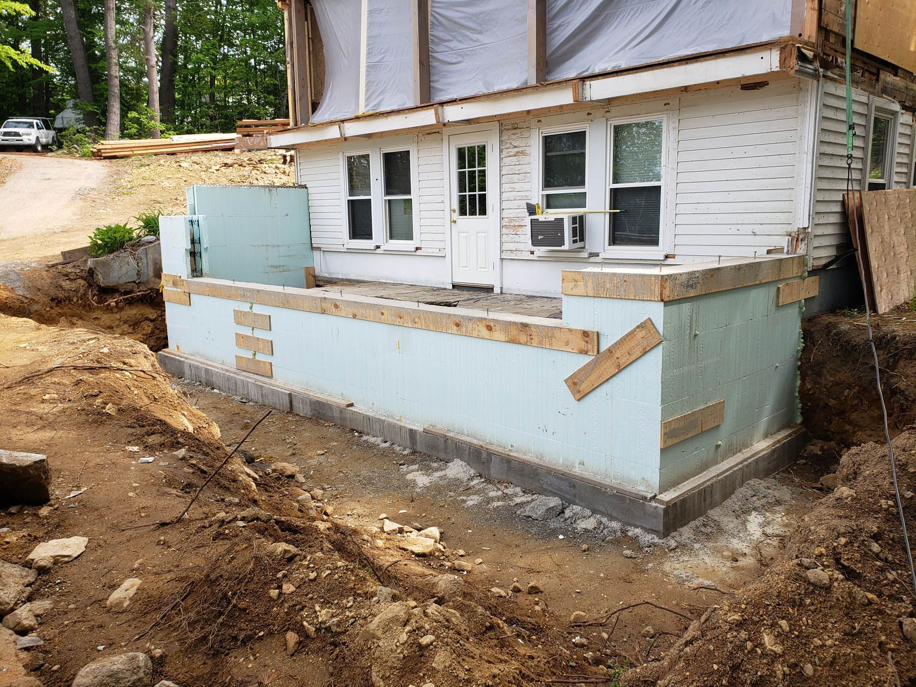 House exterior under construction, with exposed foundation, blue insulation, and dirt.