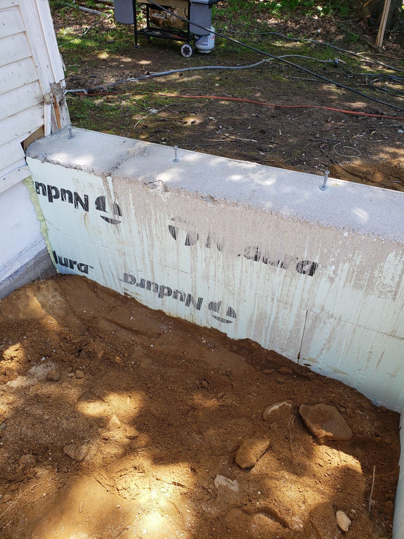 A partially constructed concrete wall with styrofoam insulation and a pile of dirt.