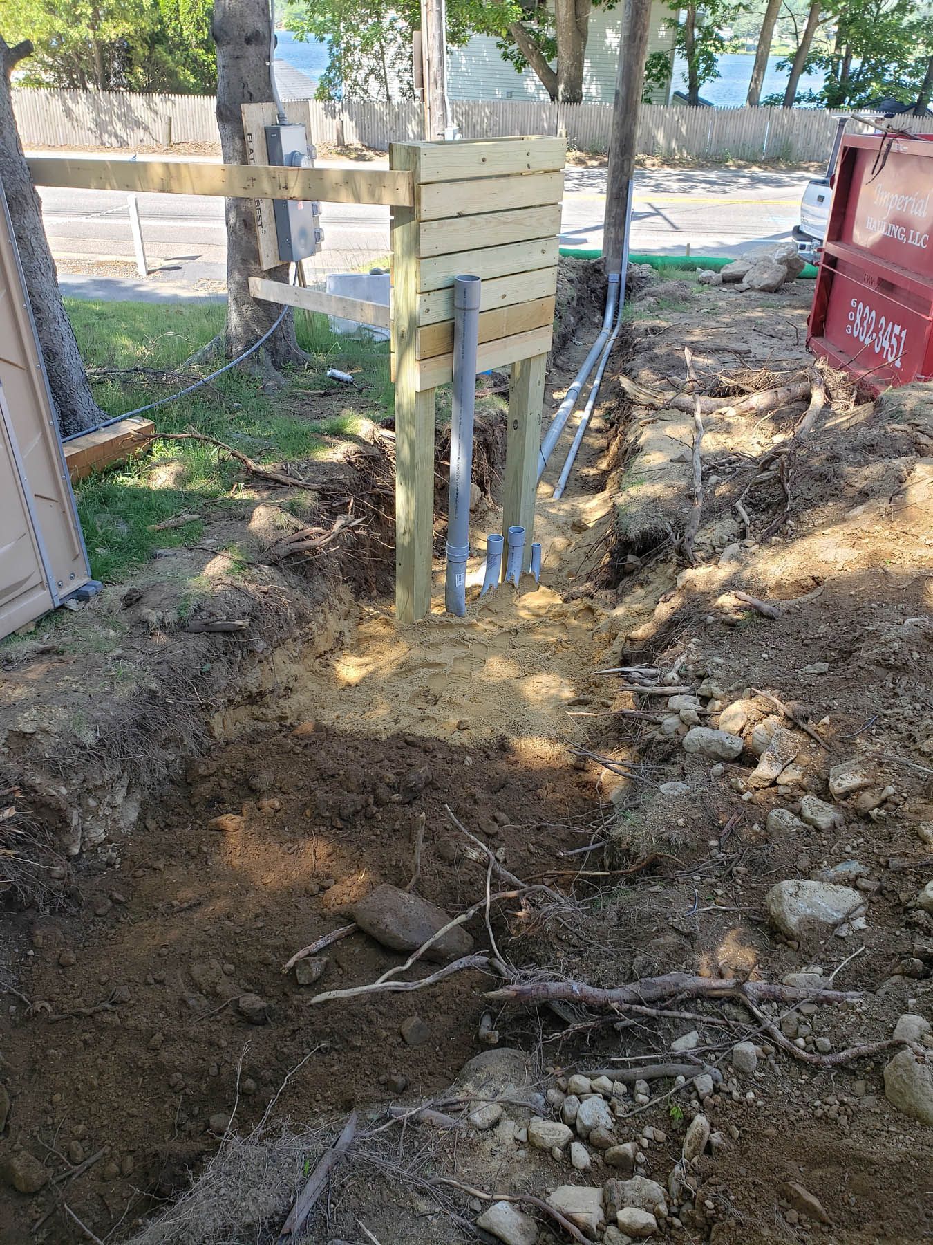 A trench dug near a wooden structure with pipes. Earth and wood are visible.