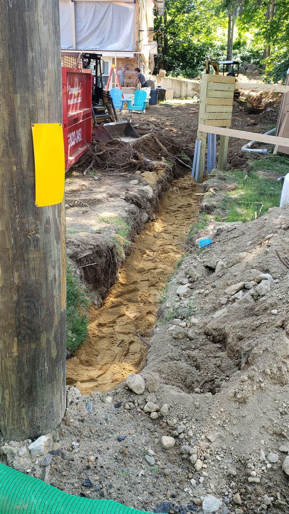Trench dug in dirt next to a utility pole with a yellow marker. Construction site.
