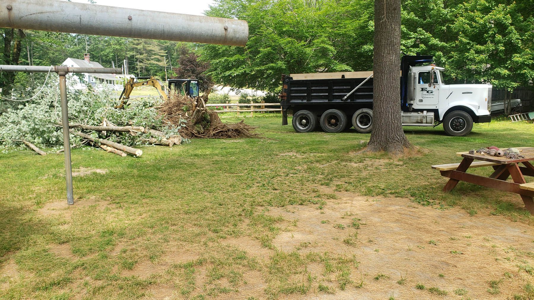 A large white dump truck parked on grass next to piles of tree branches and a picnic table.