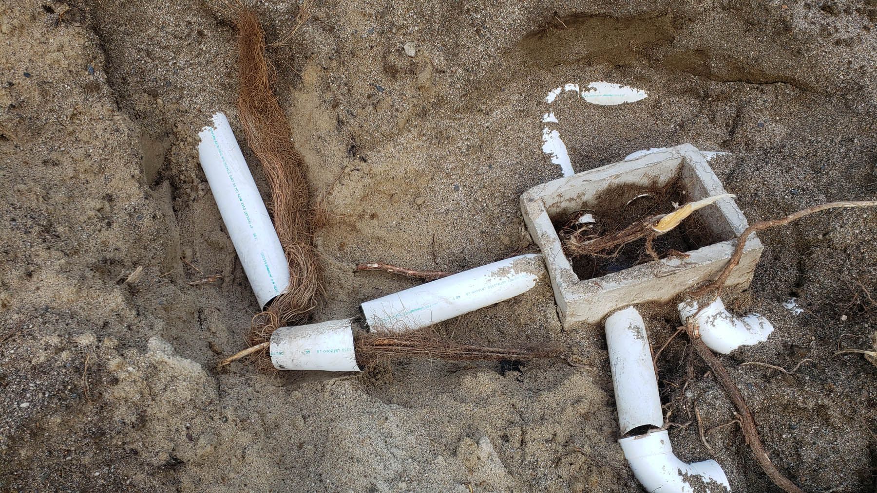 White plastic debris in sand: a square box, pipes, and cylindrical pieces.