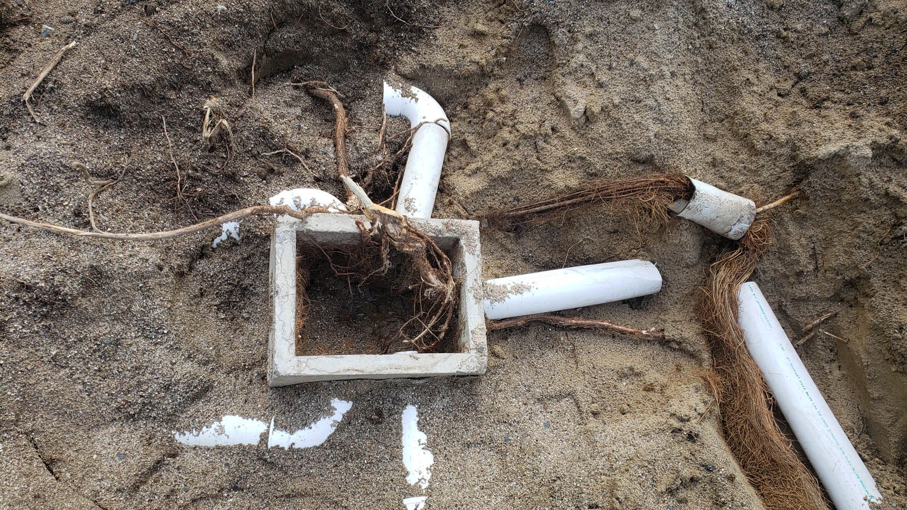 White plastic pipes and a square box partially buried in sand.