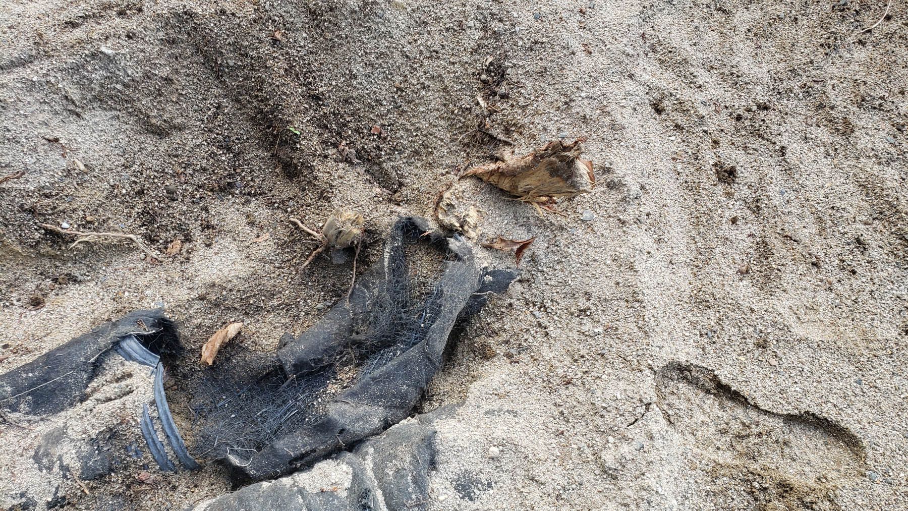 Black fabric scraps and debris on sand.
