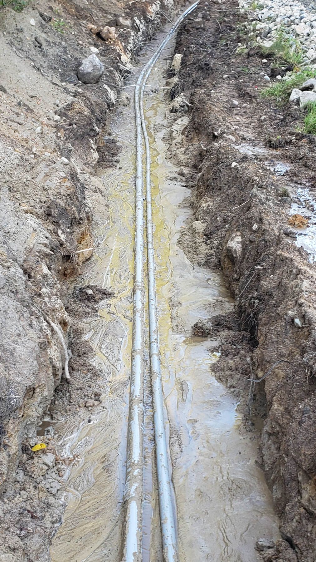 Two parallel silver pipes in a trench of brown soil.