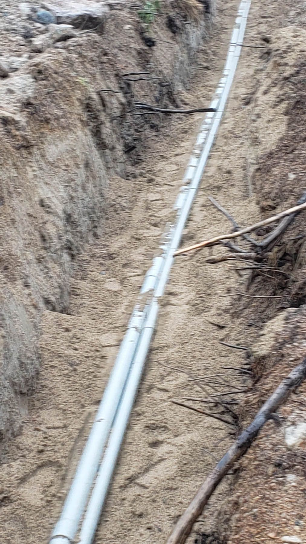 Trench with two parallel white conduits installed; dirt walls and earth setting.