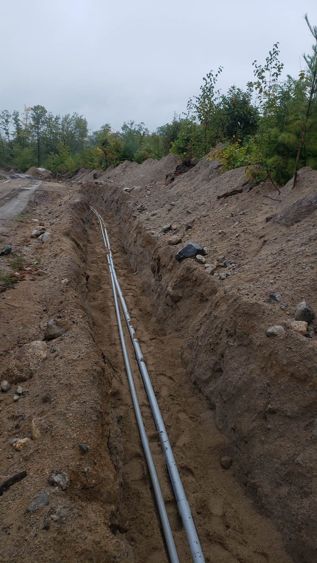 Two parallel pipes laid in a trench in a dirt landscape, under an overcast sky.