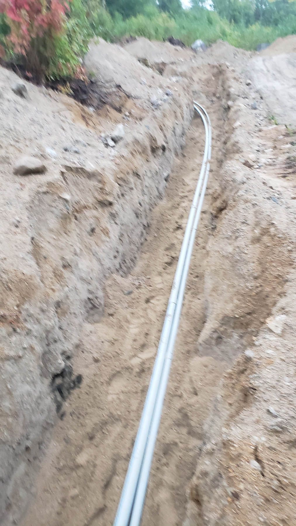 Two gray conduits run through a freshly dug dirt trench in an outdoor construction site.