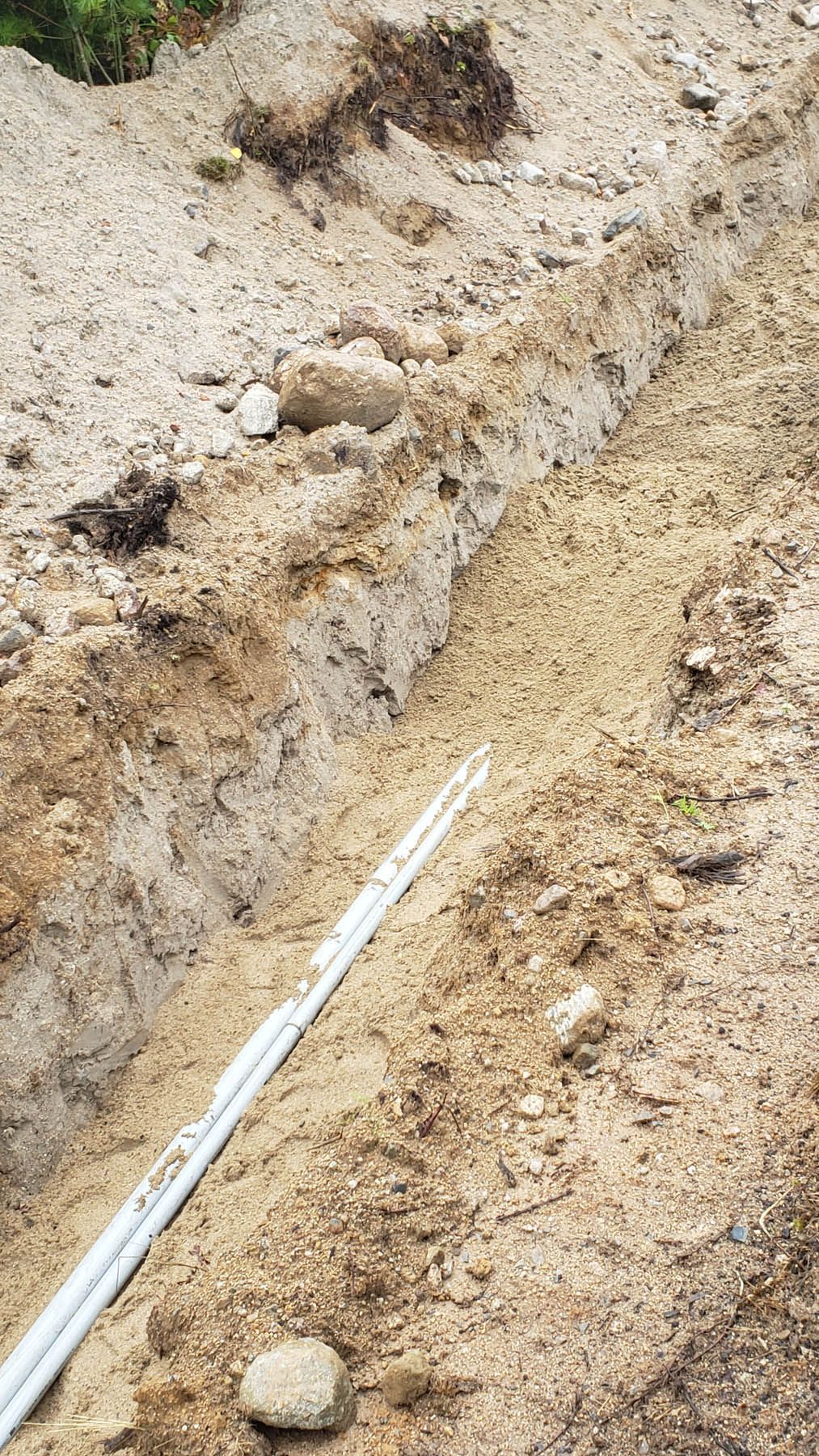 Trench dug in dirt with white pipes inside, ready for burial.