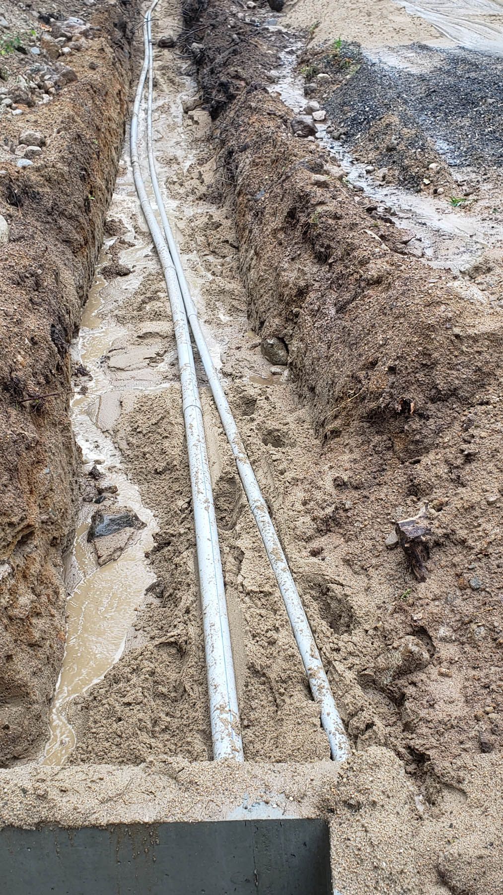 A muddy trench with two white pipes running through it, likely for utilities.