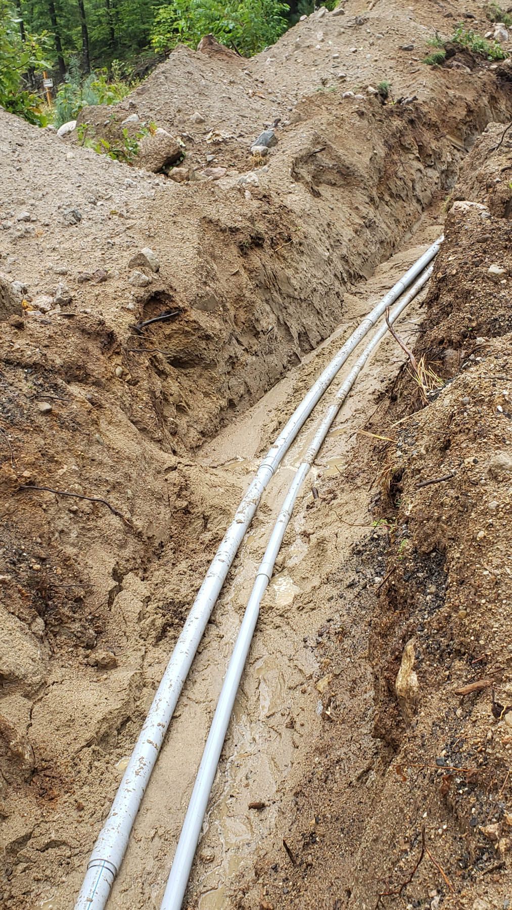 Two white pipes in a trench dug in brown soil.