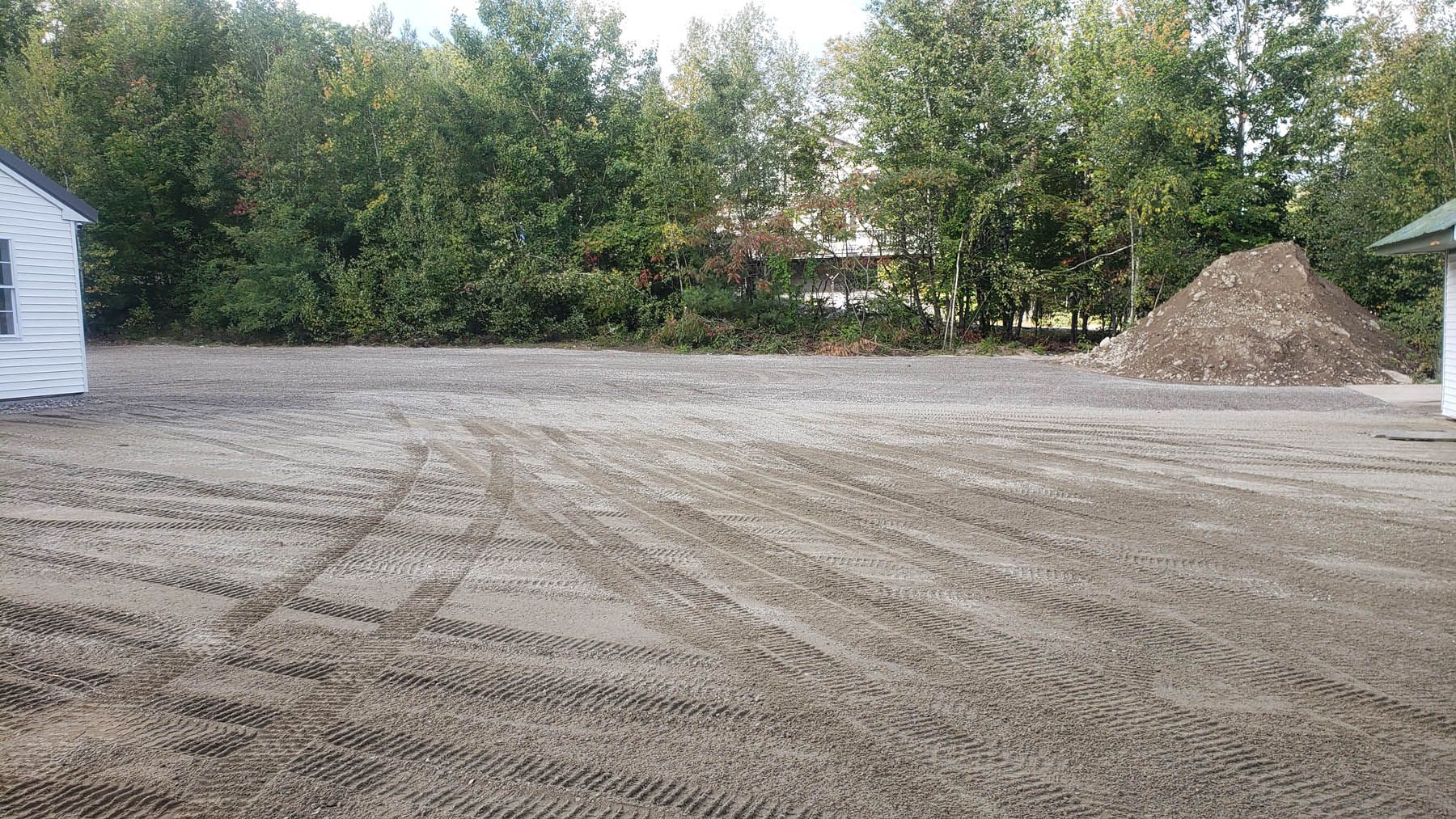 A cleared, dirt lot with tire tracks, trees in the background, and small piles of dirt.