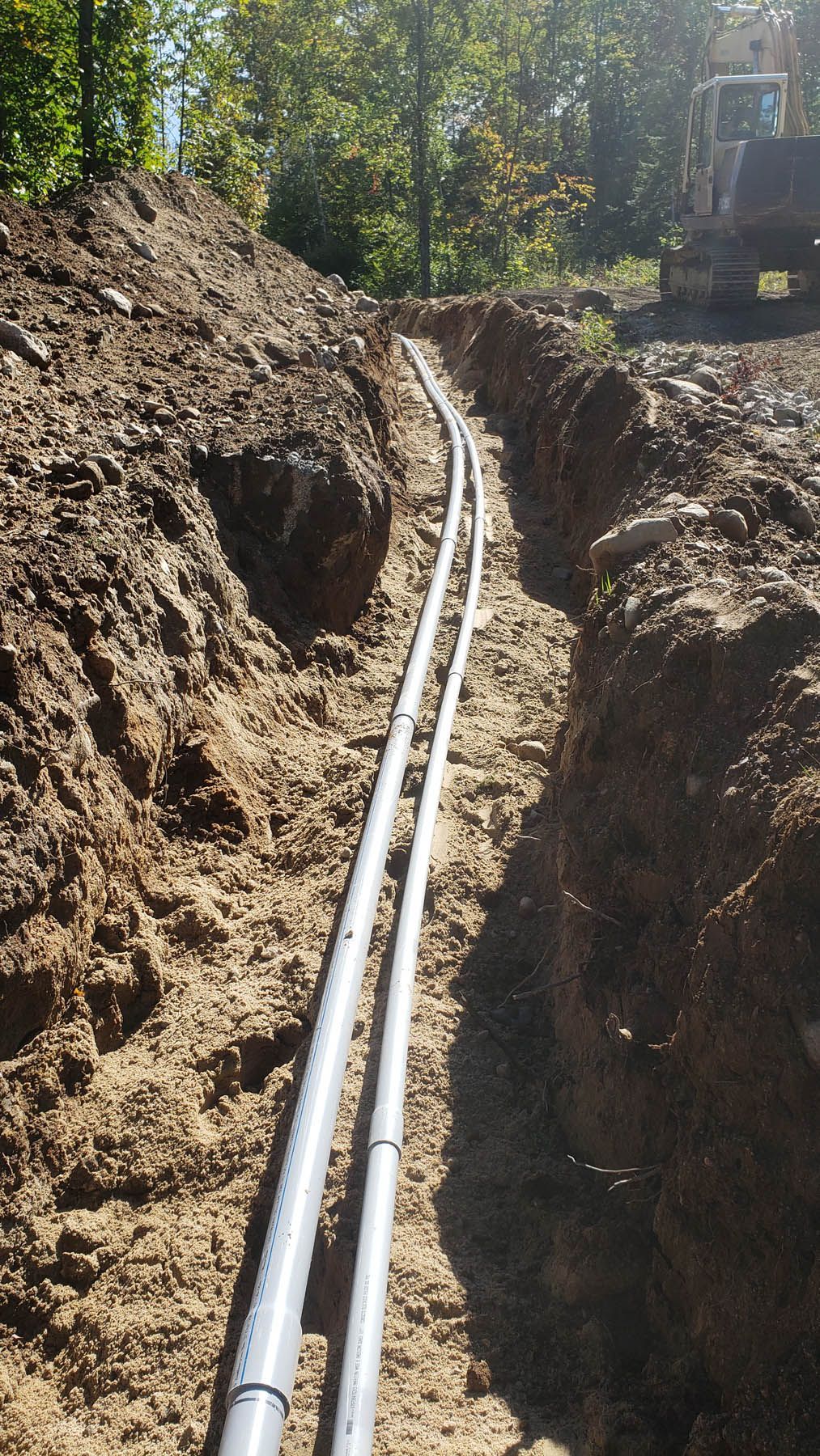 Two grey pipes in a dirt trench, likely for utilities, in a construction site.