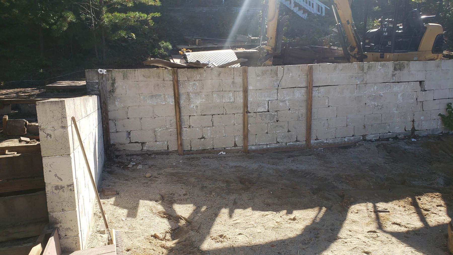 Concrete block retaining wall under construction with dirt and excavator.