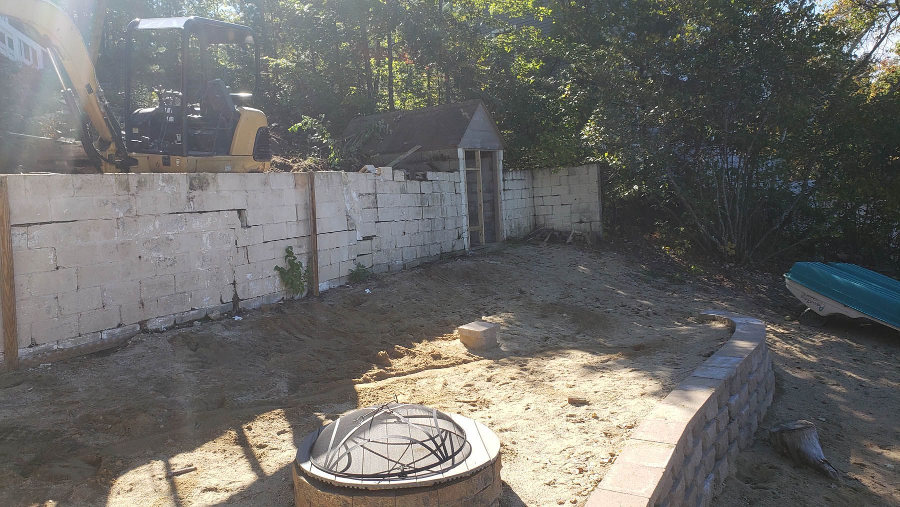 Construction site with a concrete wall, ground, and an excavator in the background.