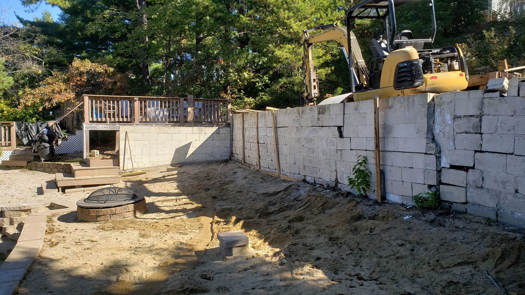 Construction site with a concrete block retaining wall, excavator, and deck.