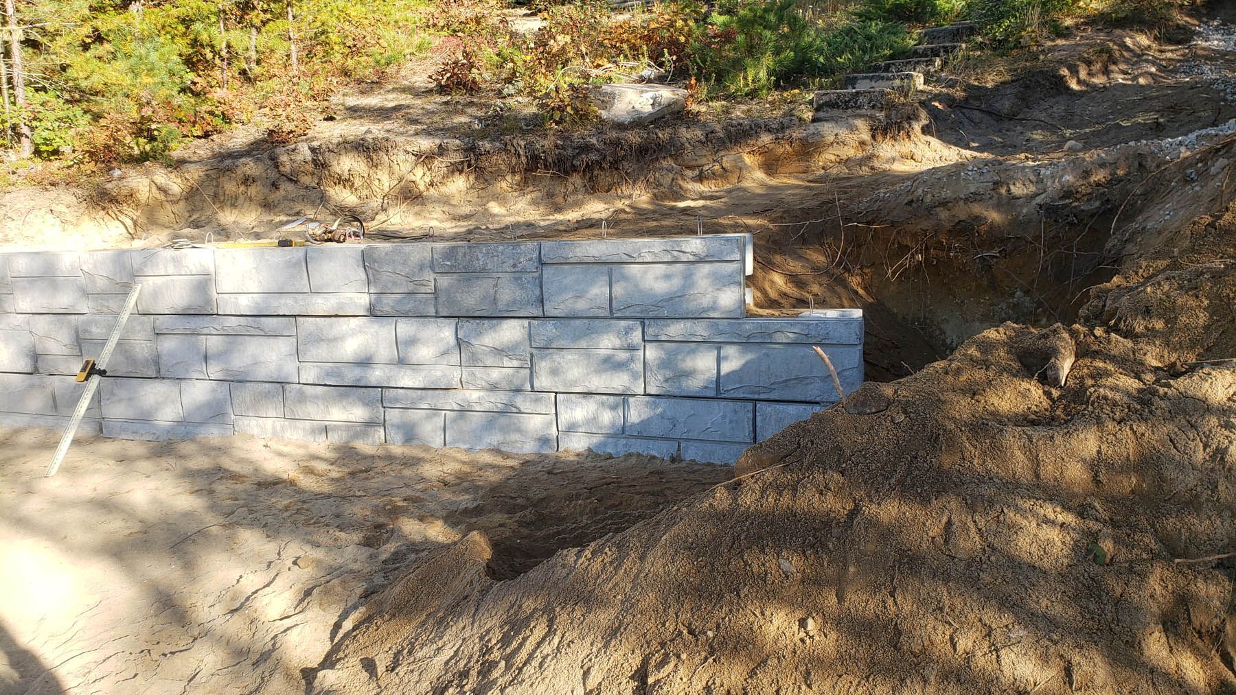 A partially built retaining wall of gray blocks in a brown dirt embankment.