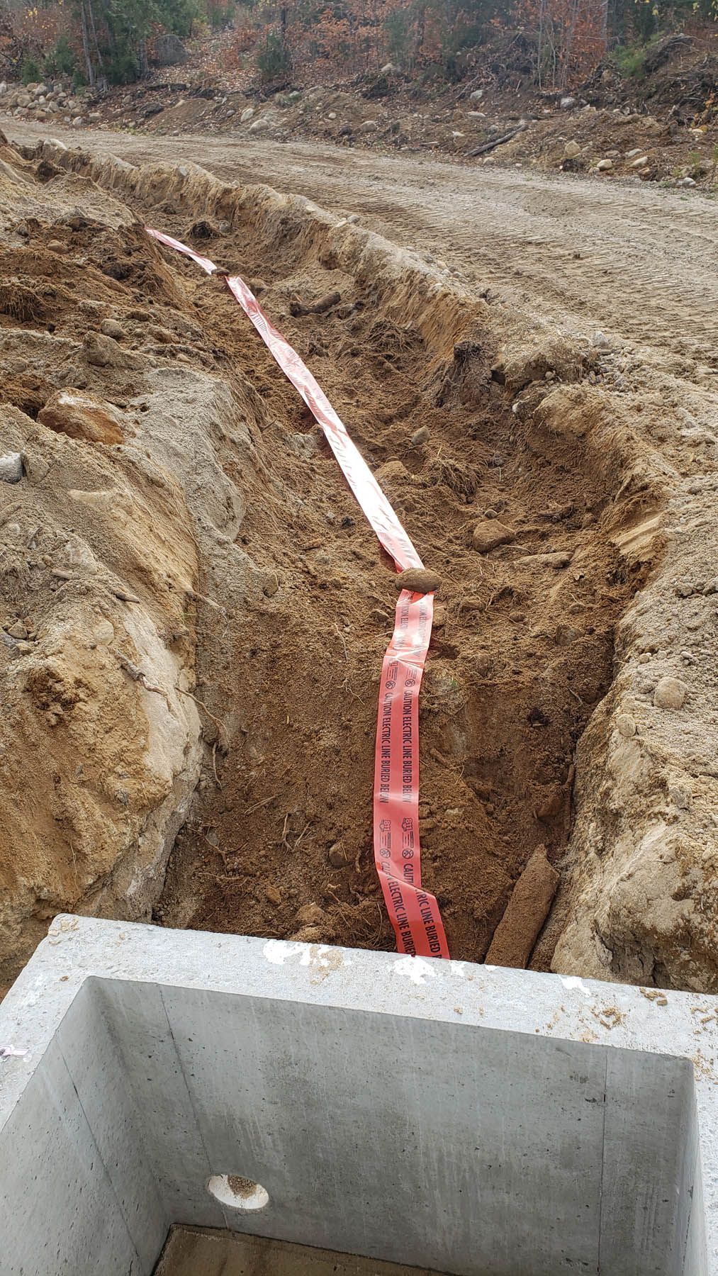 A trench with a red warning tape runs from a concrete box into the earth.