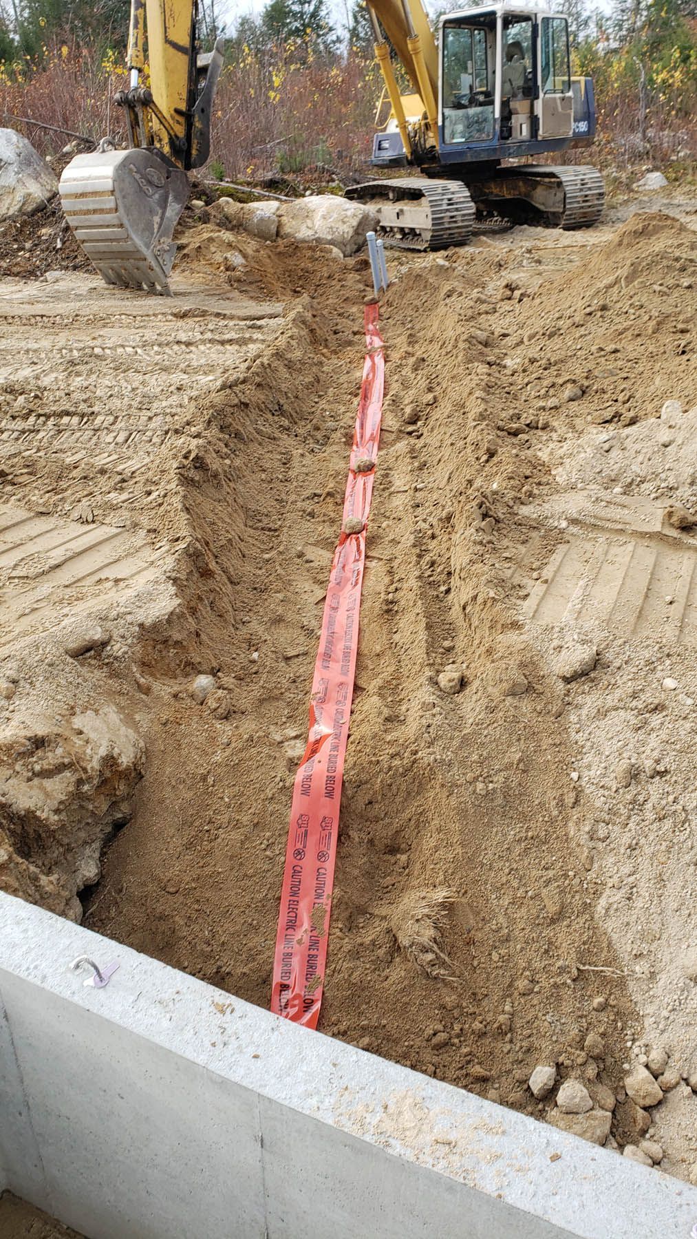 Construction site: excavator digging trench with orange safety netting.