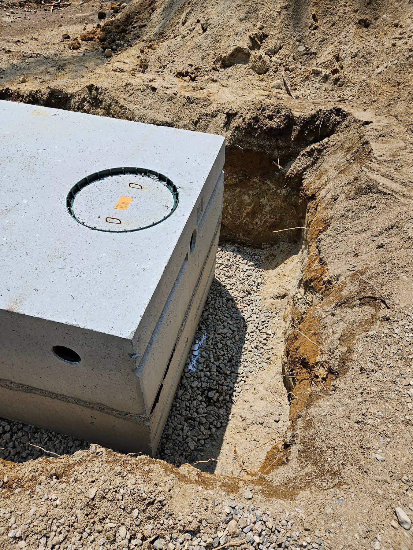 Concrete septic tank being lowered into a dug trench filled with gravel.