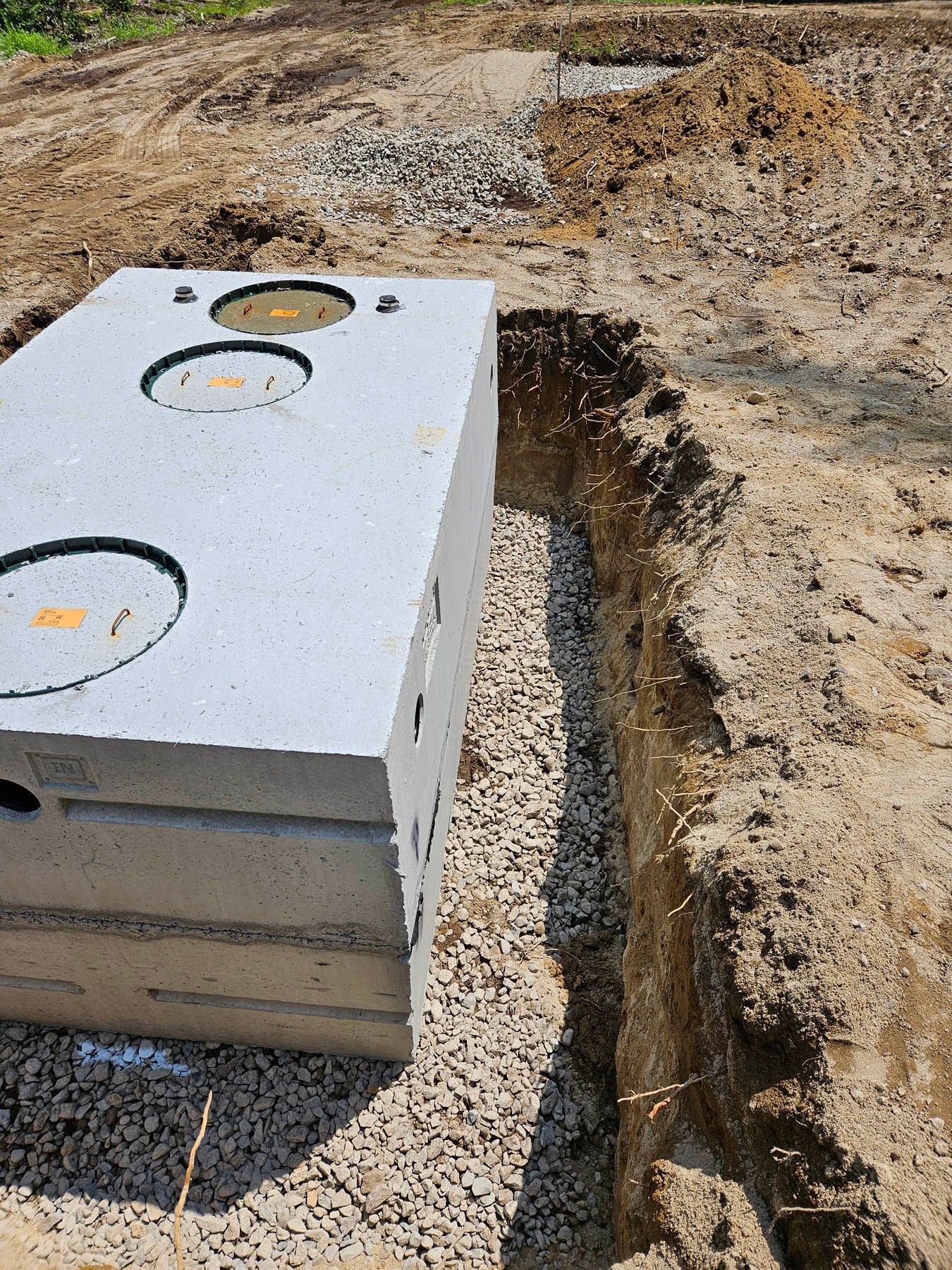 Concrete septic tank in a gravel-lined trench, ready for burial in a dirt yard.