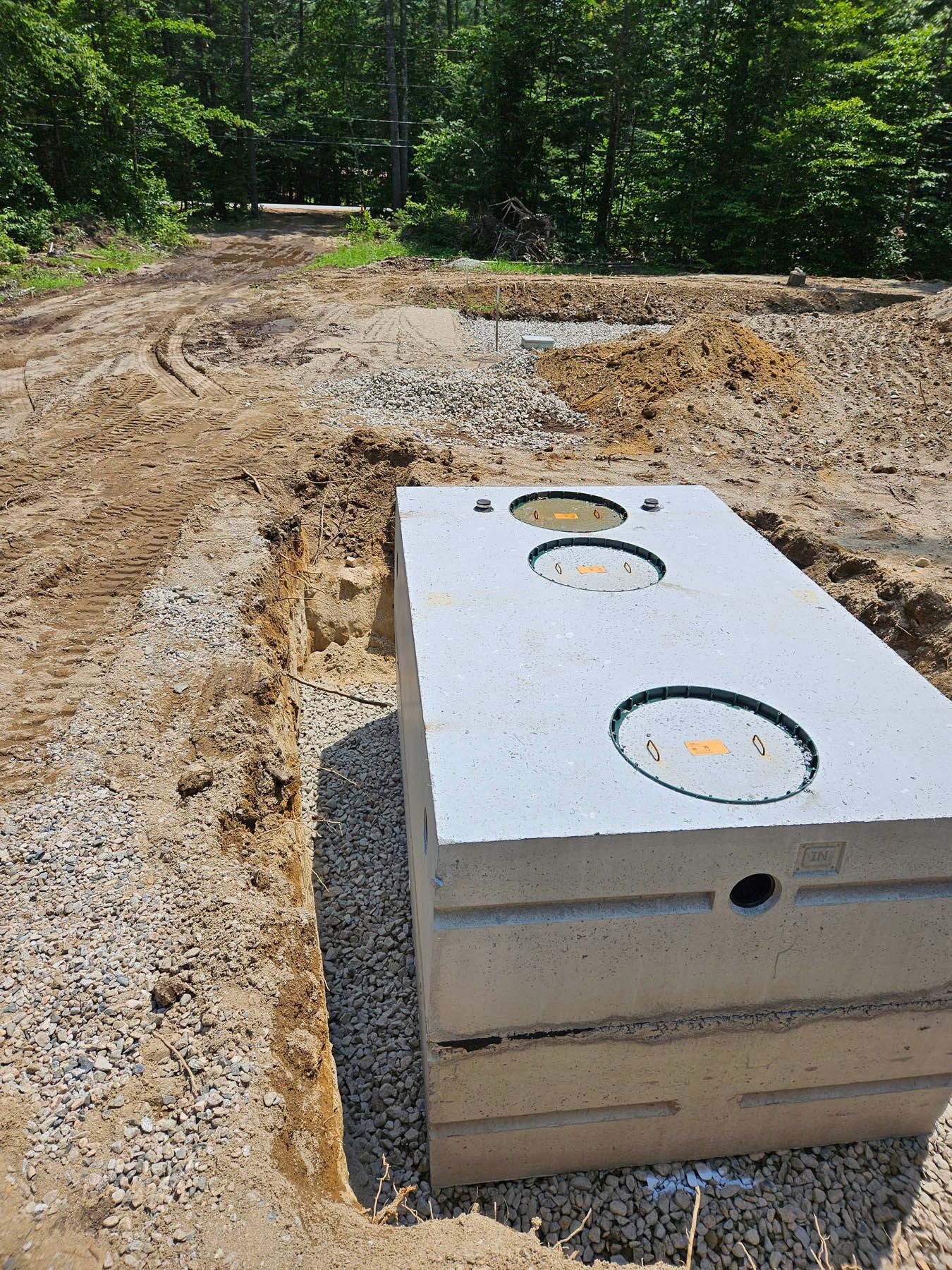 Concrete septic tank in a freshly dug trench, gravel base. Rural outdoor setting.