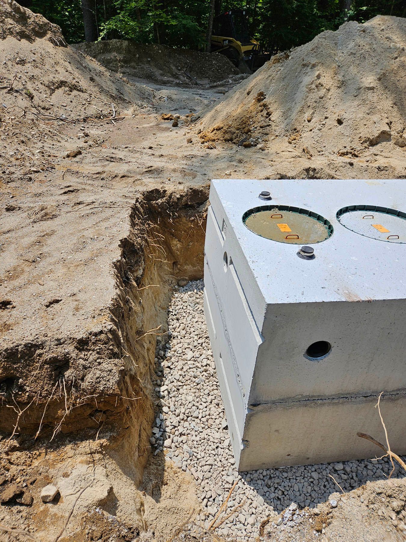 Concrete septic tank in trench, surrounded by gravel and dirt.