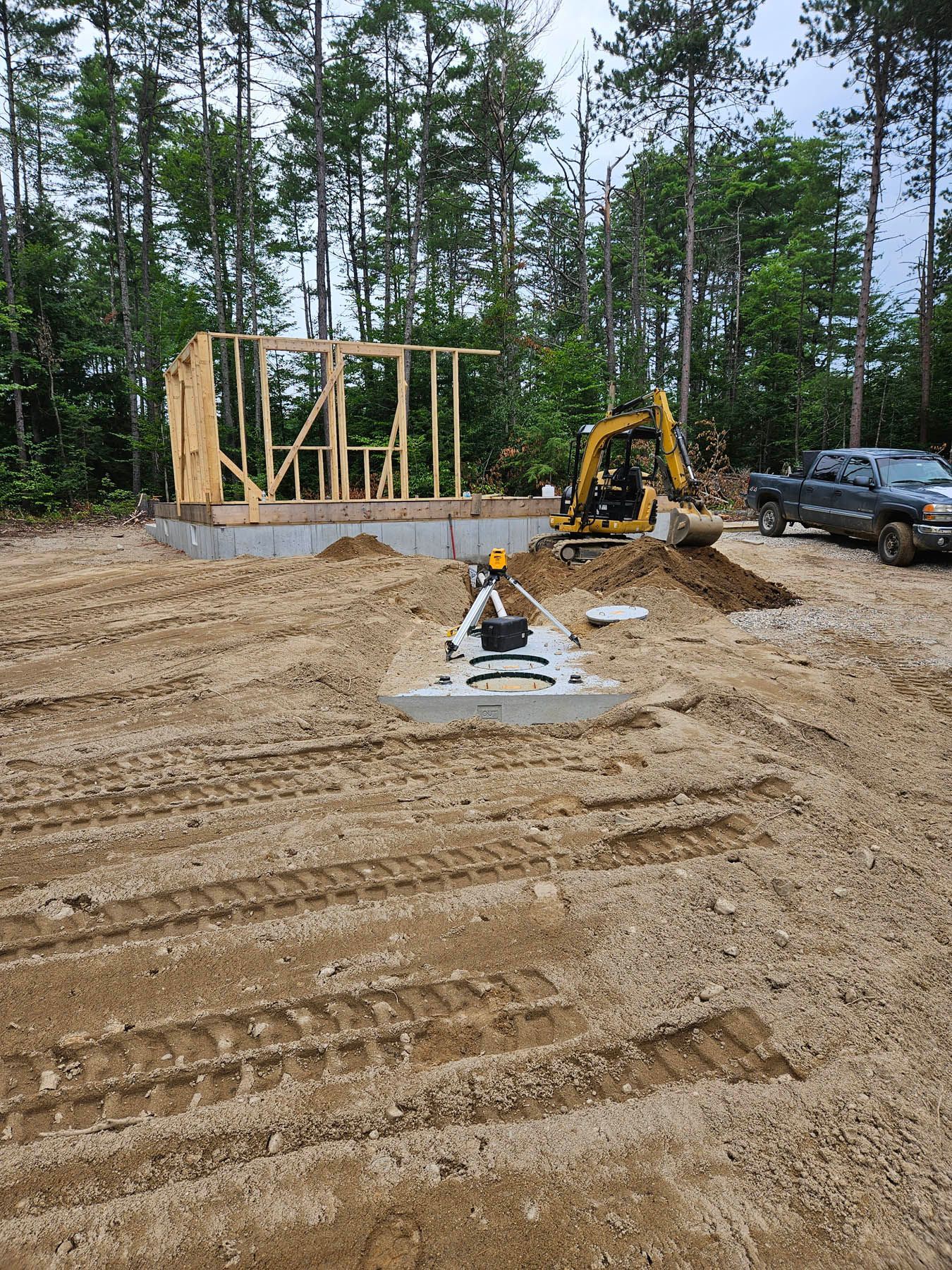 Construction site with partially built wooden frame structure. Excavator and truck in dirt.