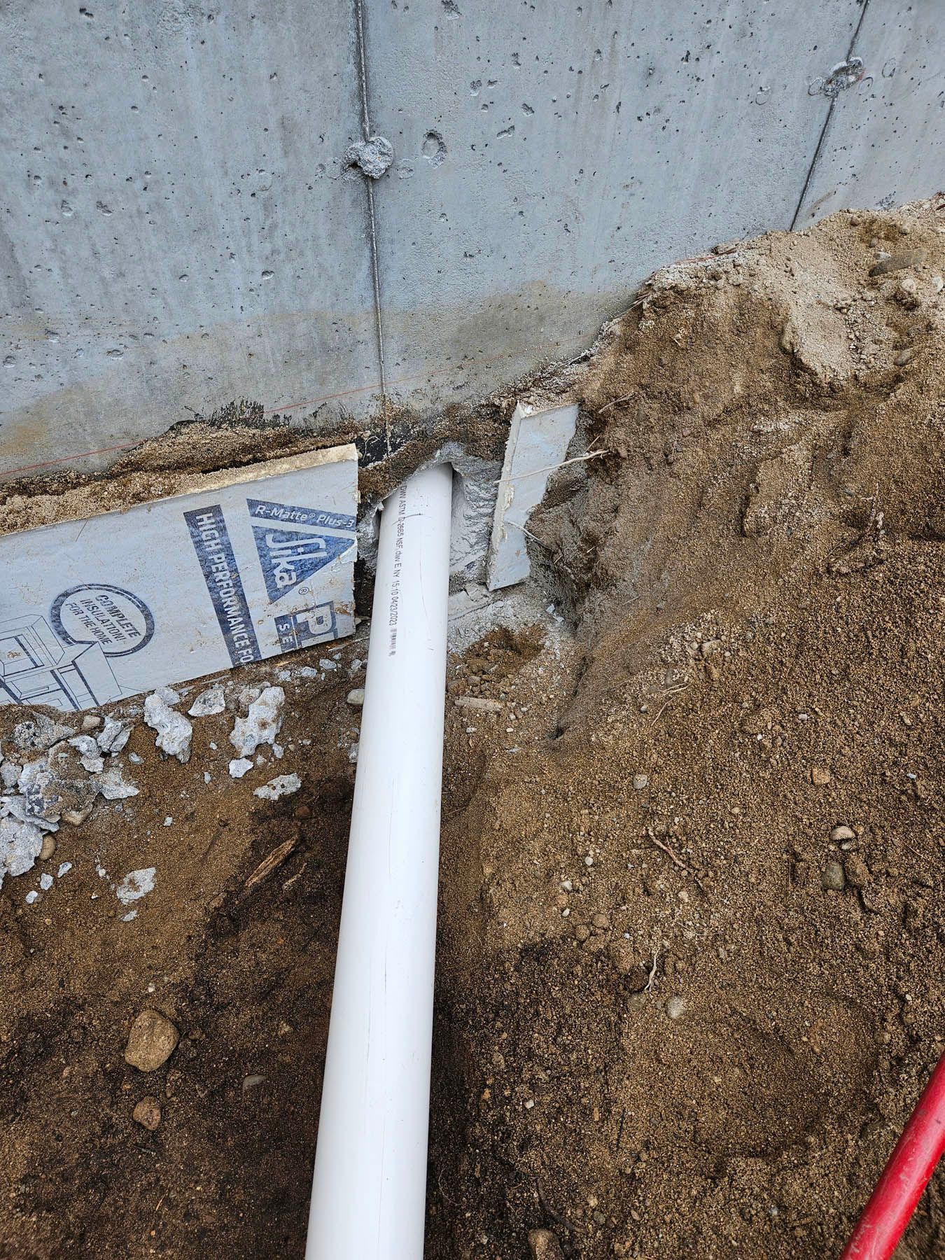 White pipe extending from a concrete foundation through dirt and insulation.
