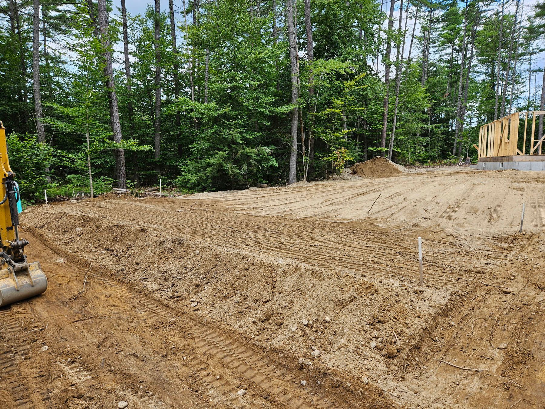 A construction site with freshly dug soil, a small excavator, and a partially built wooden structure.