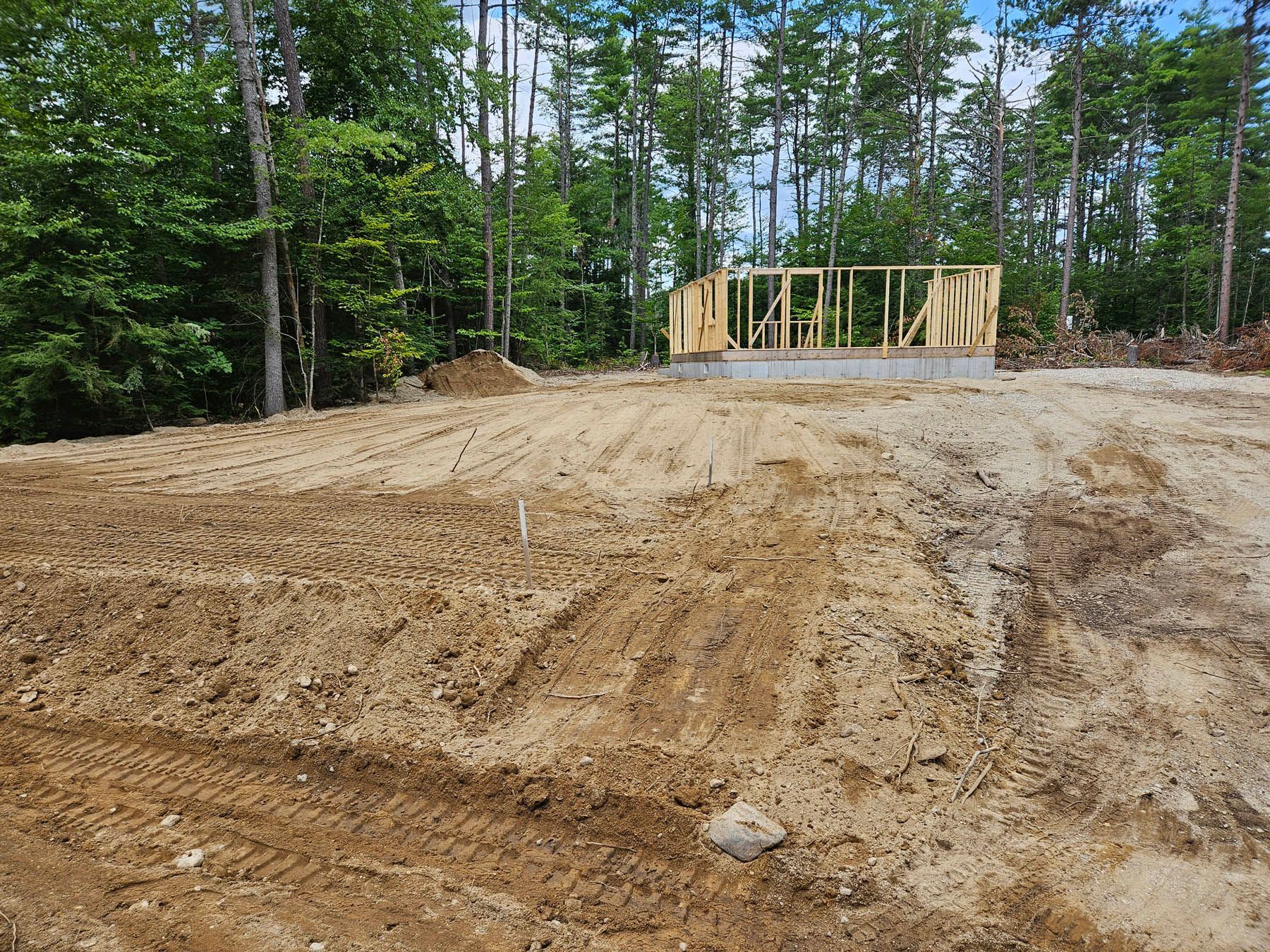 Construction site: foundation with wooden frame, dirt lot, trees in background.