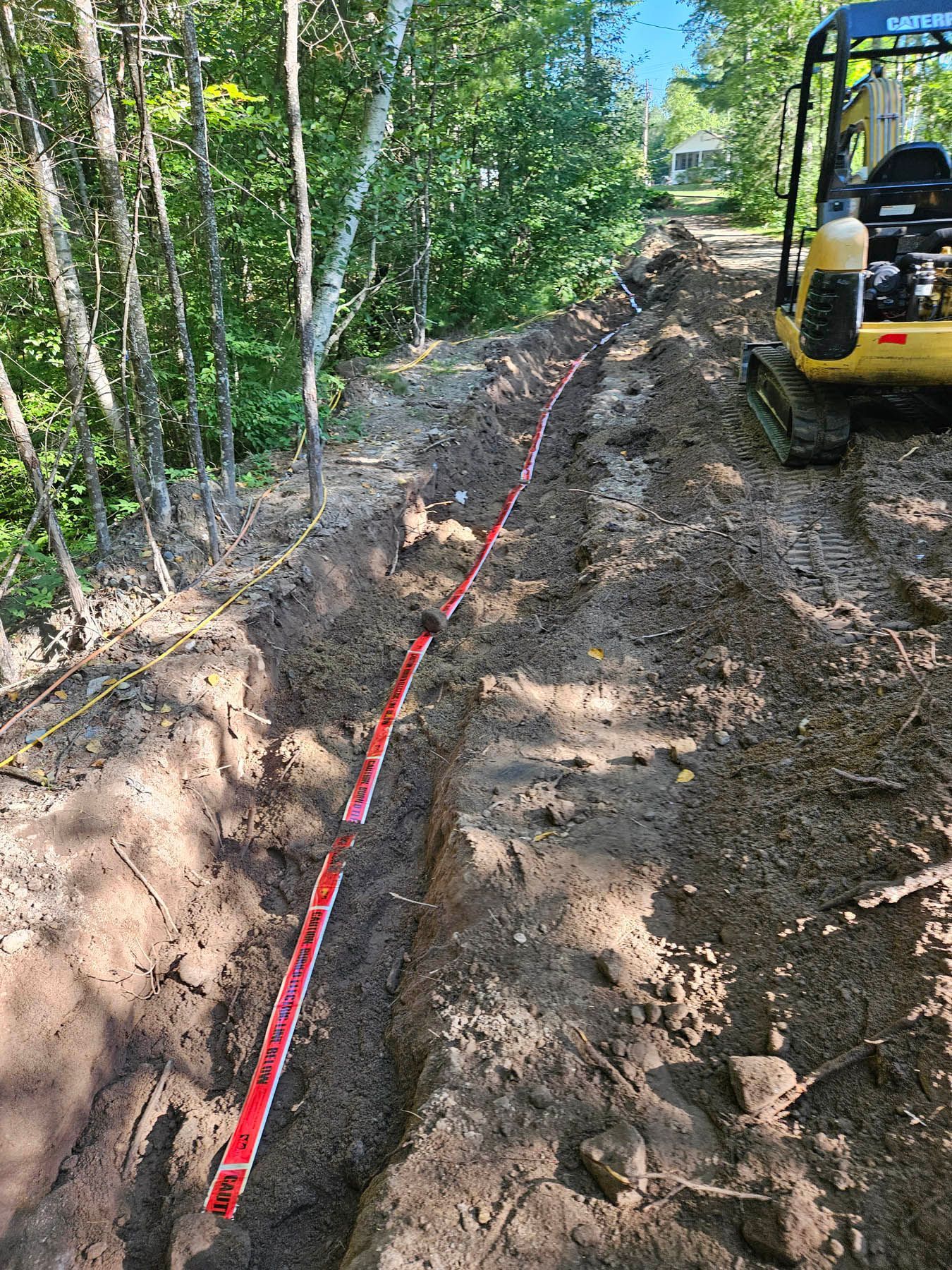 Trench dug on a hillside with a red guide, next to trees and an excavator.