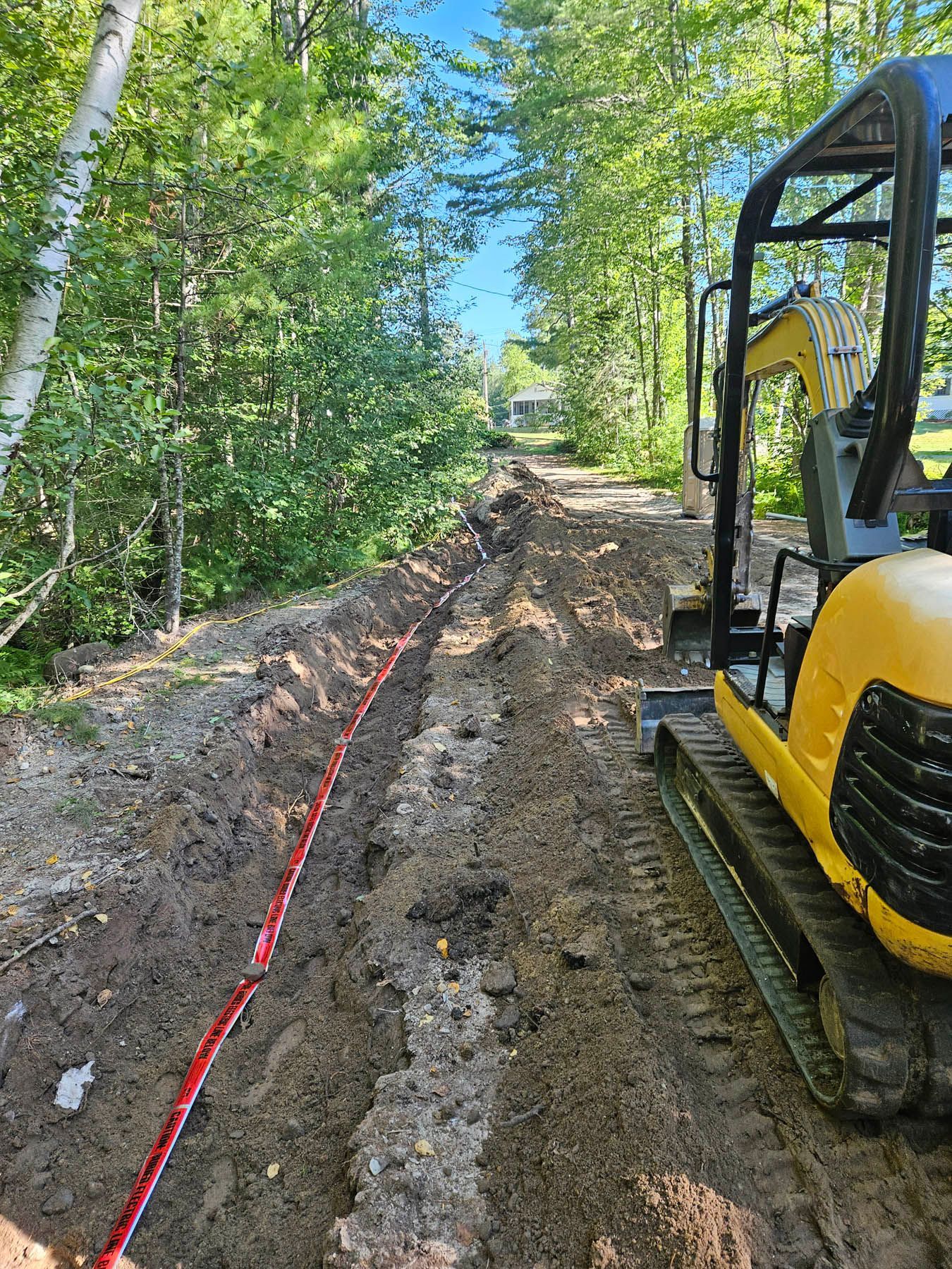 A small excavator digging a trench in a dirt path, a red cable lies inside.