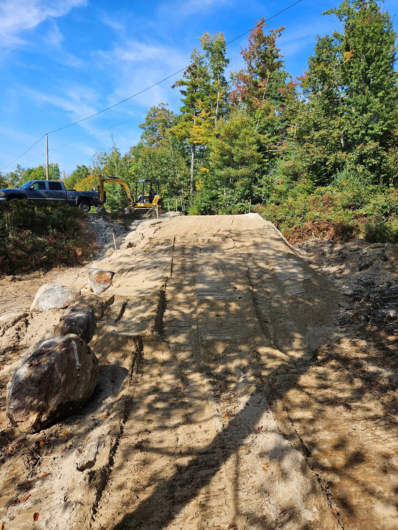 Dirt bike jump in a wooded area under a blue sky.