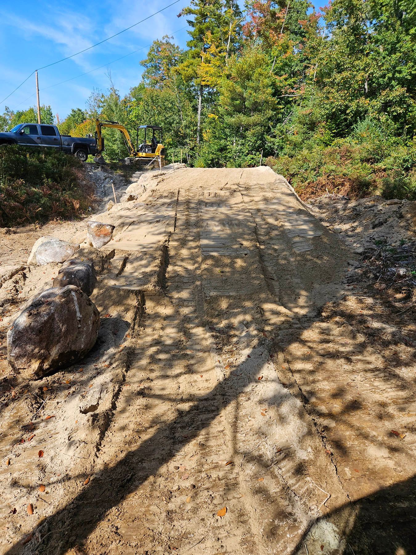 Dirt ramp for bikes or vehicles, outdoors. Brown soil, sunny day, green trees in the background.