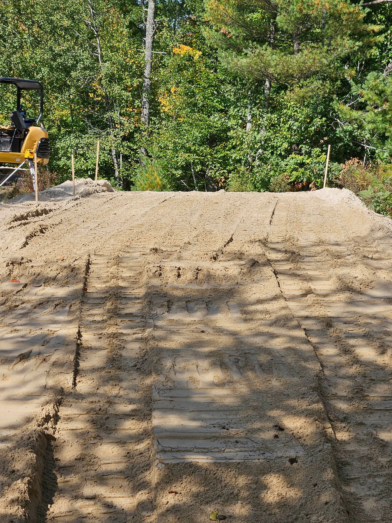 Dirt pile with marks, surrounded by trees. Construction site setting.