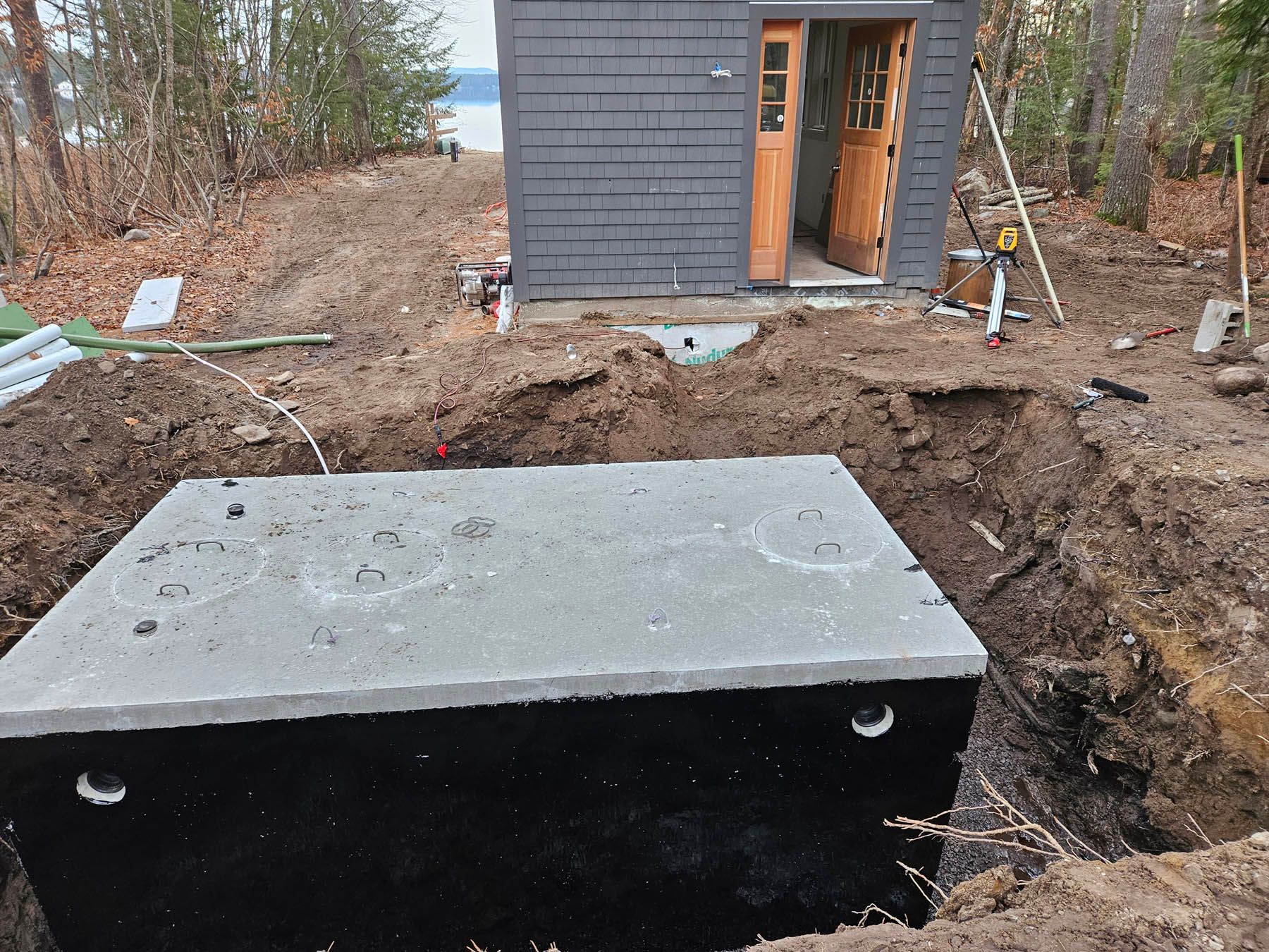 A concrete septic tank installed in a dirt excavation near a small building.