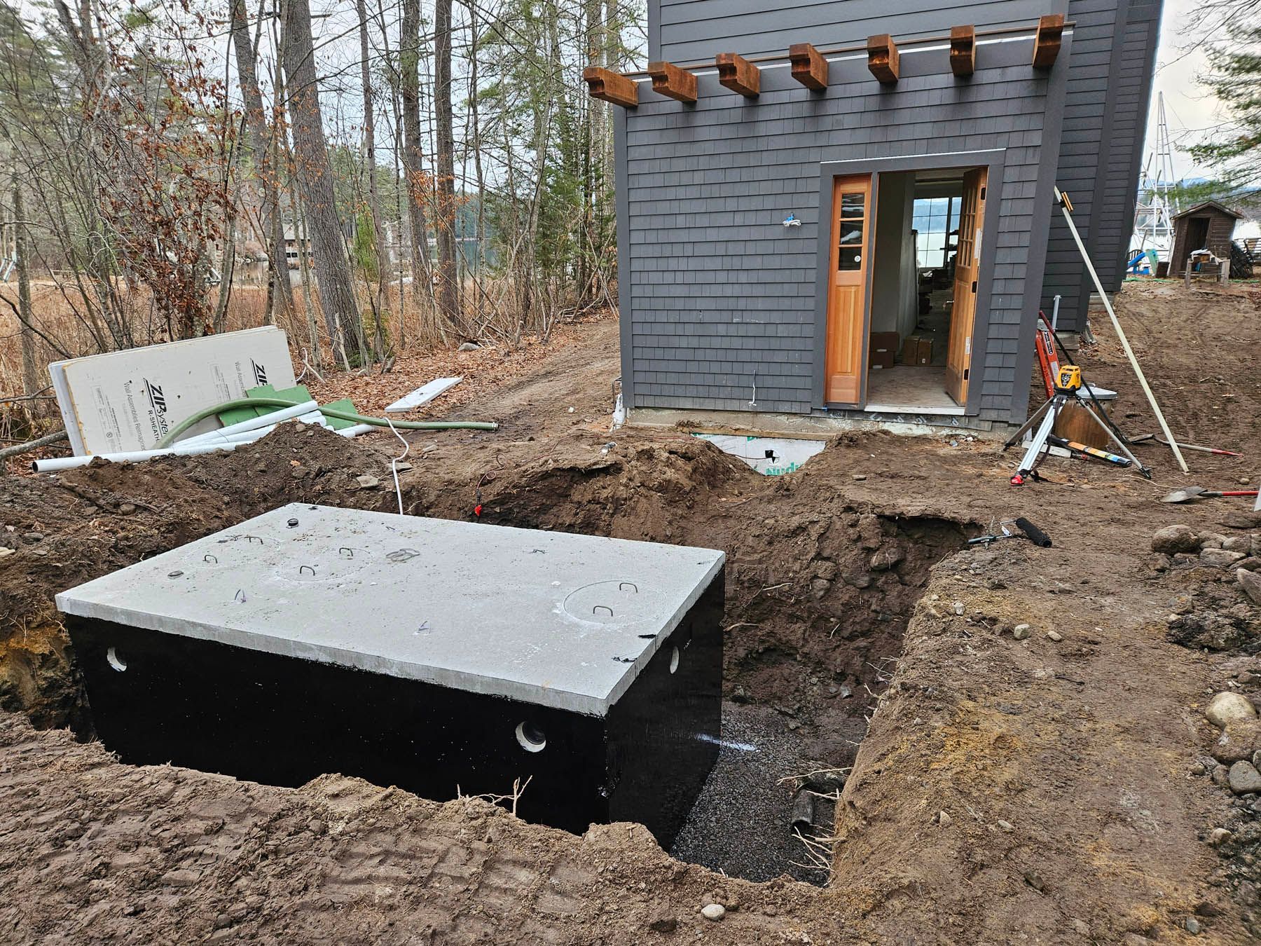 A concrete septic tank sits in an excavated area near a dark-colored building with open doors.