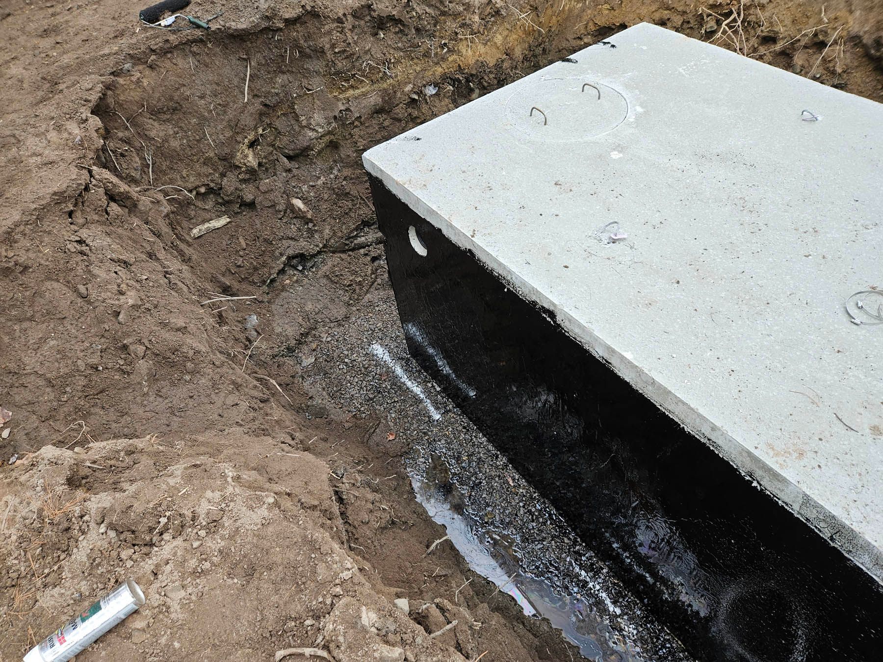 Concrete septic tank in a trench, coated in black sealant, ready for burial.