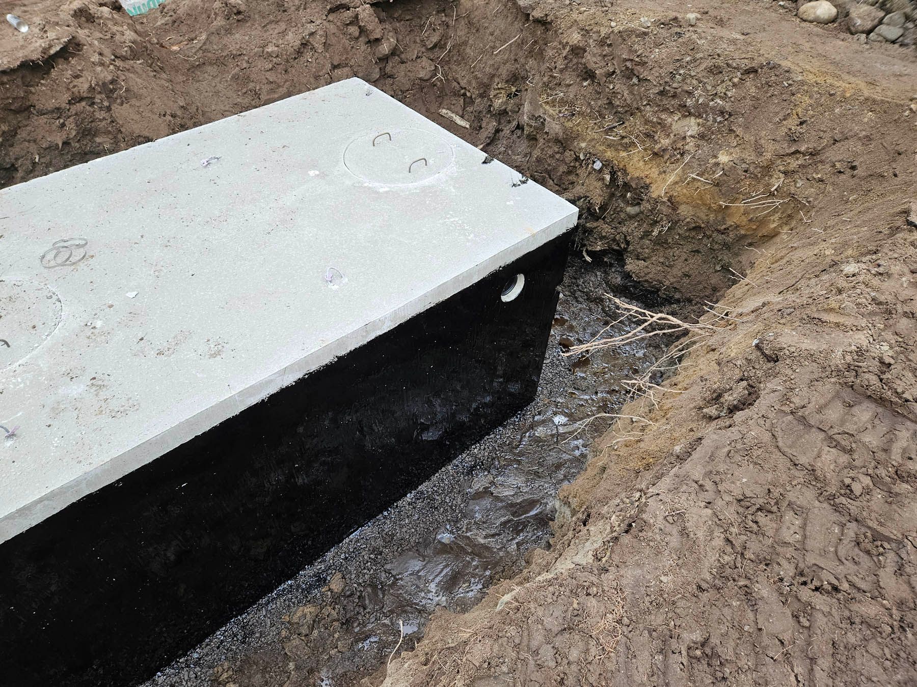 A concrete box with a lid sits partially buried in a dirt trench.
