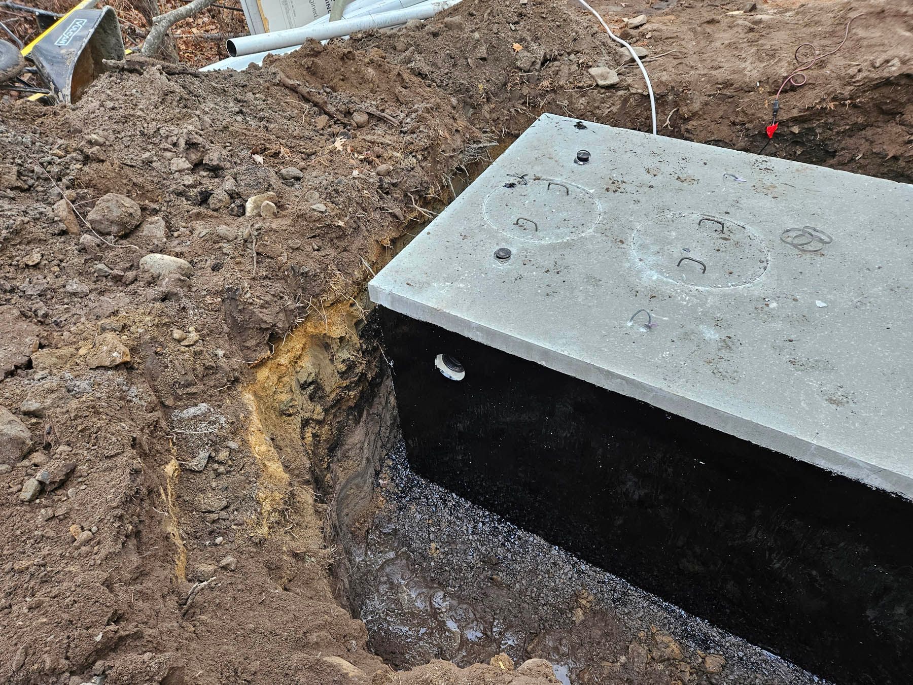 Concrete septic tank in a dirt excavation, partially buried, lid visible.
