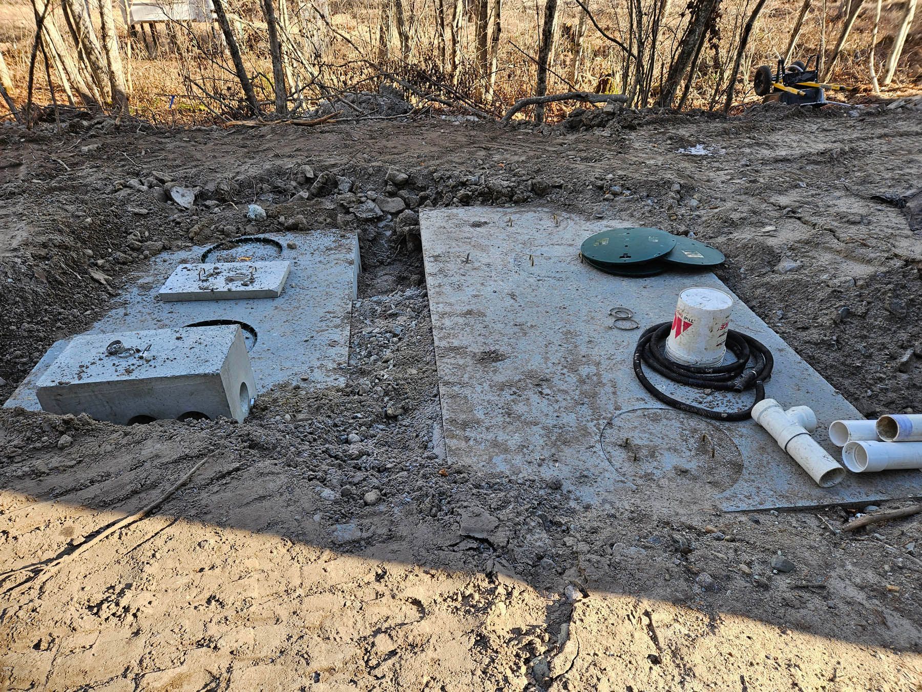 Open septic tank installation site with concrete lids, piping, and tools in a dirt field.