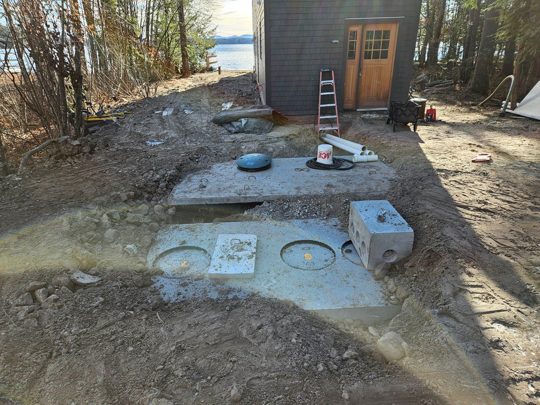 Septic system installation near a small dark building, outdoor construction site.