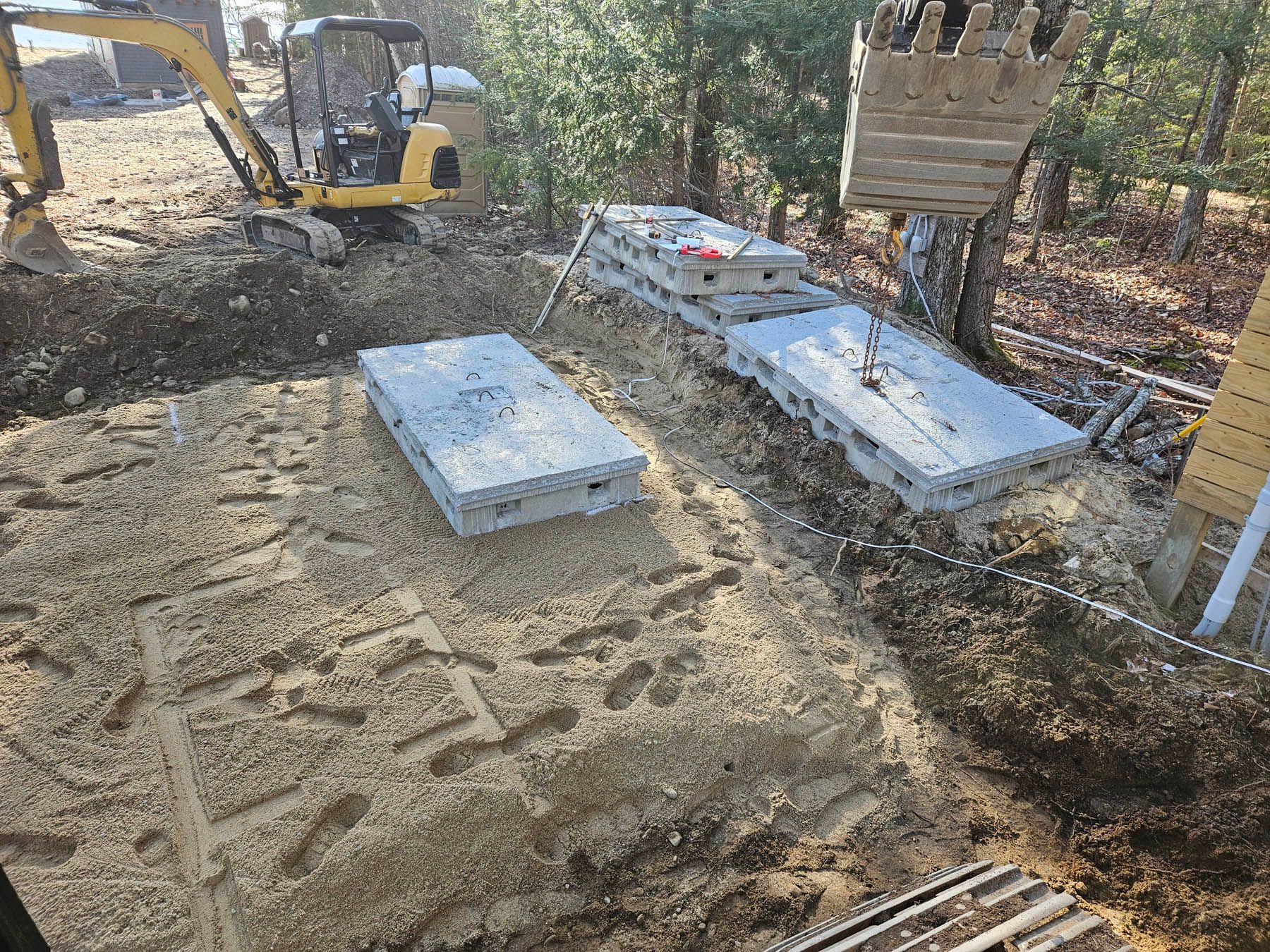 An excavator places concrete slabs in a gravel-filled pit. Construction site with a forest background.