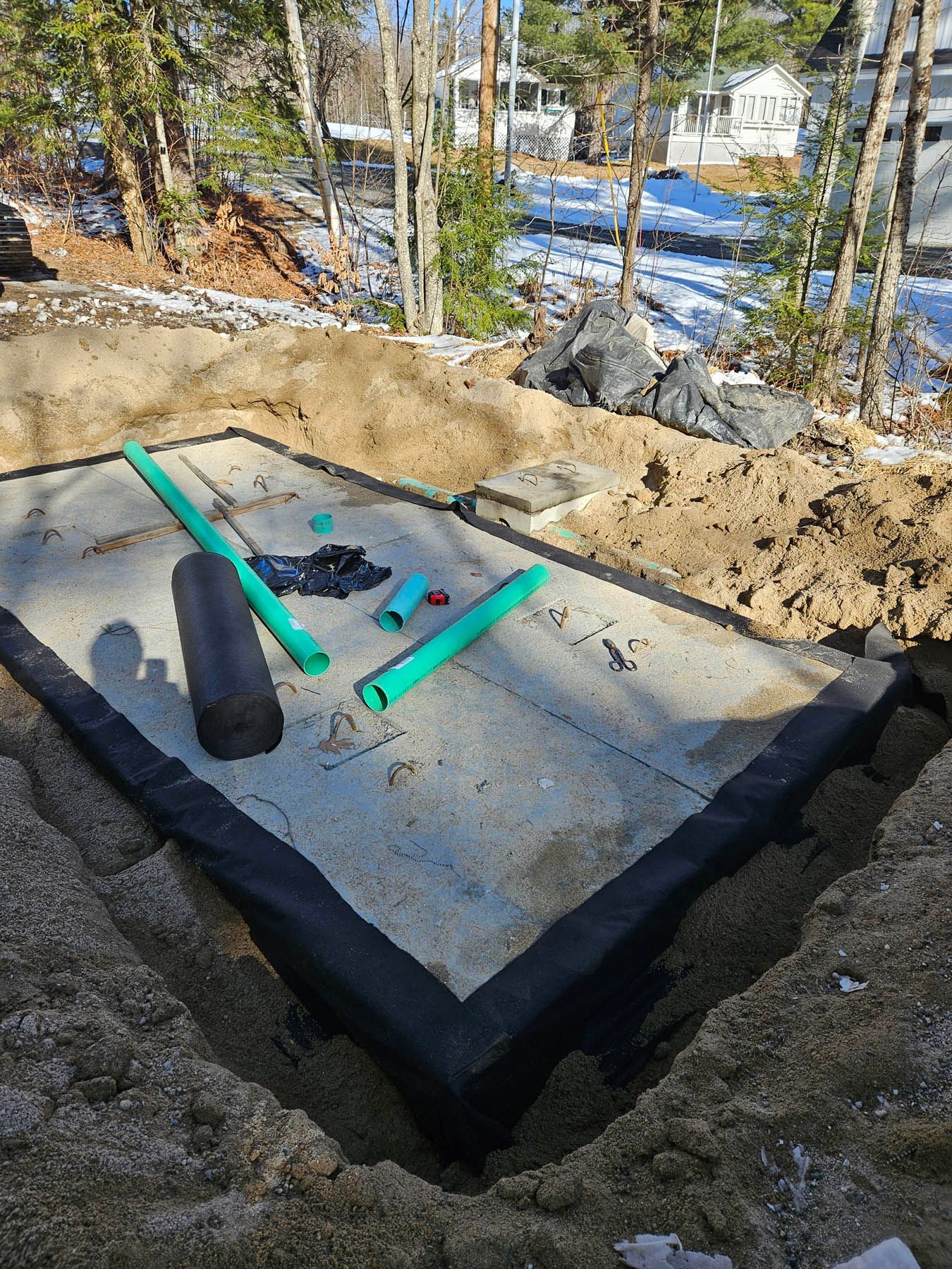 Concrete septic tank with green pipes in a dug-out area, outdoors. Construction site setting, winter.