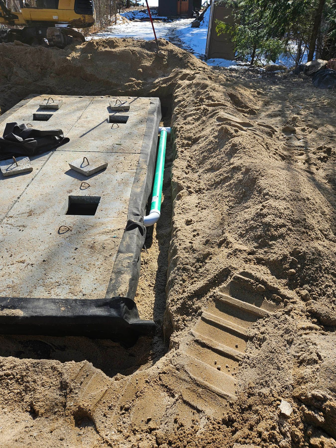 Concrete septic tank with green pipe in a sandy trench during installation.