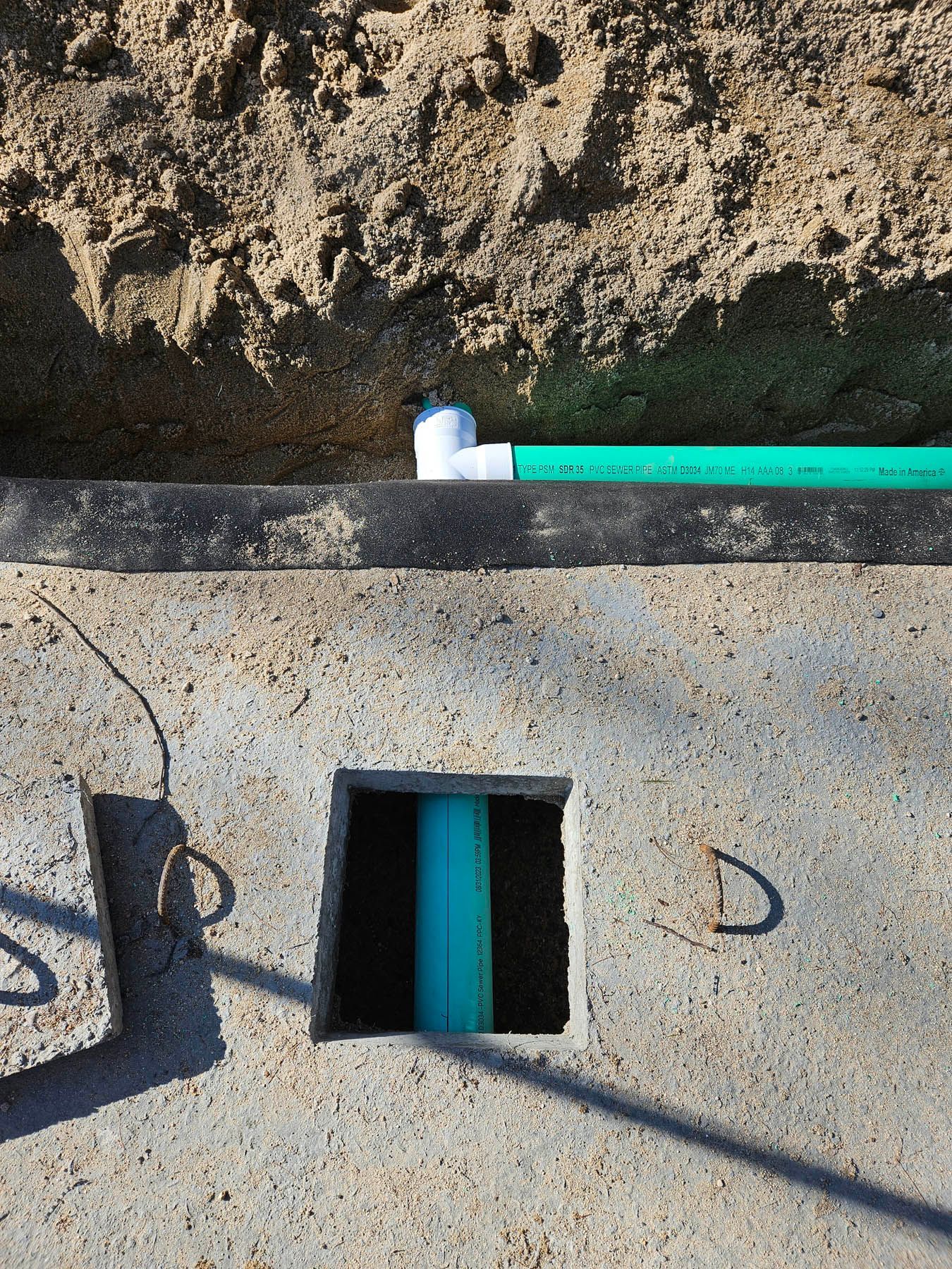 A concrete slab with a hole containing blue pipe, connected to a green pipe; dirt in the background.
