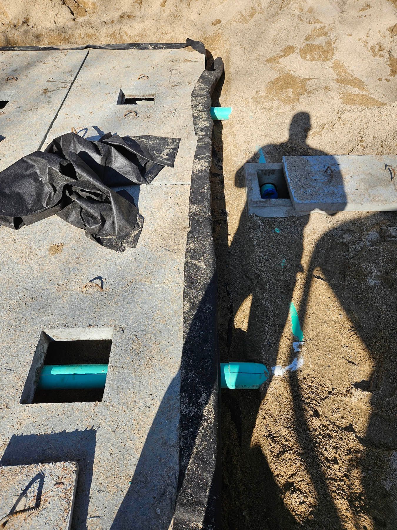 Construction site with concrete covers, exposed pipe, and a trench in the sand.